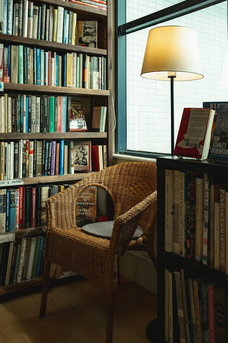 Cozy reading nook with a wicker armchair and bookshelf by the window.