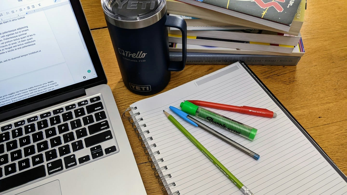 Laptop, coffee mug, and stationery arranged on a wooden desk.